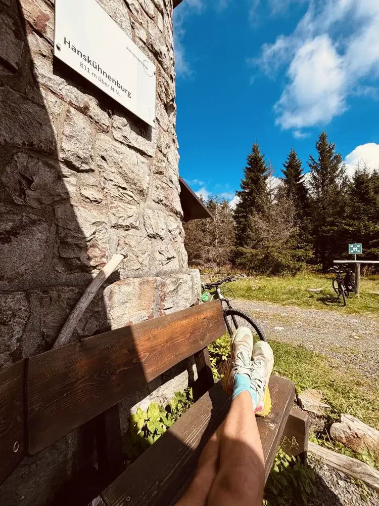 Rast auf der Bank an der Hanskühnenburg, am Turm das Schild 811 m über N.N., daneben ein Fahrrad