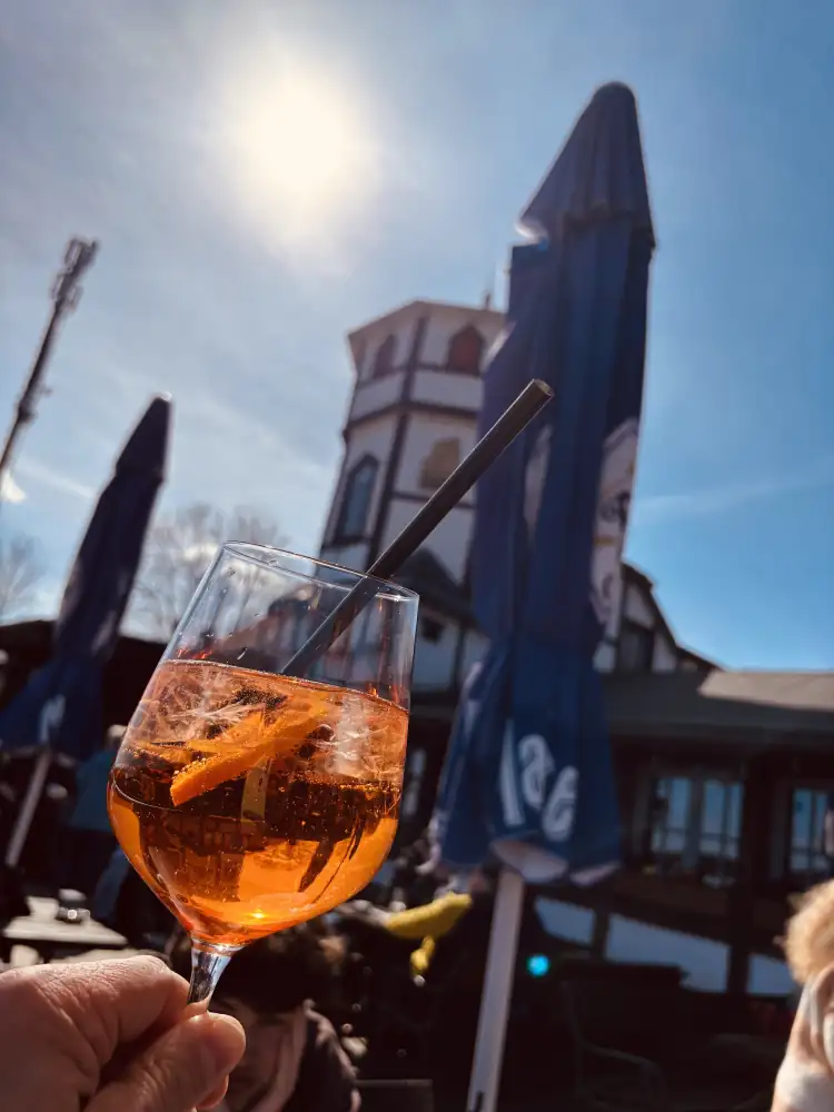 Aperol Spritz auf der Sonnenterrasse der Berggaststätte Hausberg, dahinter der Turm